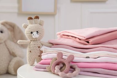 İçerideki beyaz masada temiz bebek kıyafetleri ve oyuncaklar yığını, yakın plan.