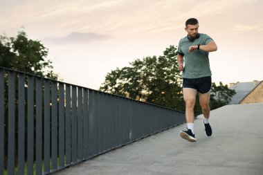 Spor giyim sektöründe sporcu genç bir adam koşuyor ve spor takip cihazını açık havada kontrol ediyor.