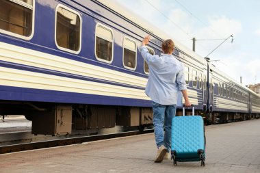 Hoşçakalın. Tren istasyonu peronunda el sallayan bagajlı adam.