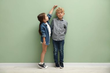 Sevimli küçük kız ve oğlan boylarını yeşil duvarın yanında ölçüyorlar.