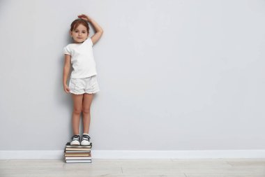 Kitap yığınının üzerinde boyunu ışık duvarının yanında ölçen sevimli küçük bir kız. Metin için boşluk