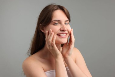Gri arka planda yüzüne krem süren güzel bir kadın.