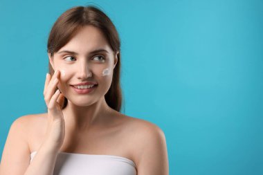 Güzel bir kadın açık mavi arka planda yüzüne krem sürüyor. Metin için boşluk