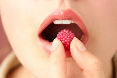 Güzel dudaklı, makyajlı ve ahududu şekerli bir kadın. Yakın plan.