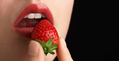 Dudak makyajı ve siyah arka planda çilek olan güzel bir kadın, yakın plan. Metin için boşluk