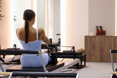 Pilates stüdyosunda, arka planda reformcular üzerinde egzersiz yapan bir kadın. Metin için boşluk