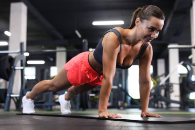 Gülümseyen kadın spor salonunda yoga minderinde kalas egzersizi yapıyor.