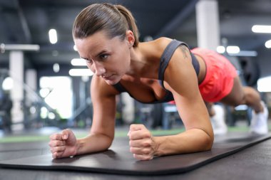 Atletik kadın spor salonunda yoga minderi üzerinde kalas egzersizi yapıyor.