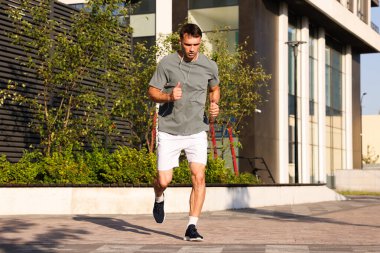 Kulaklıklı bir adam güneşli bir günde dışarıda koşuyor.