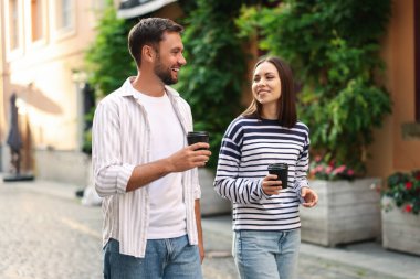 Paket kahve. Kağıt bardaklı bir çift şehirde yürüyor.