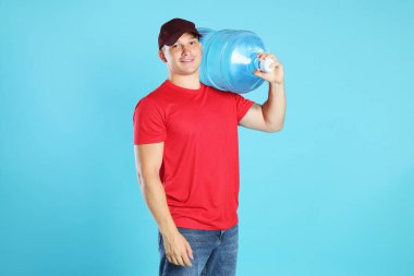 Açık mavi arka planda soğuk su şişesiyle gülümseyen teslimatçı.