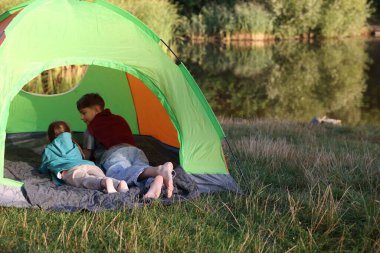 Erkek ve kız kardeş nehir kenarındaki kamp çadırında çıplak ayakla dinleniyorlar. Metin için boşluk
