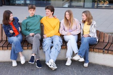 Bir grup genç dışarıda bankta oturuyor.