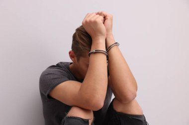 Açık gri duvarın yanında metal kelepçeli bir adam var.