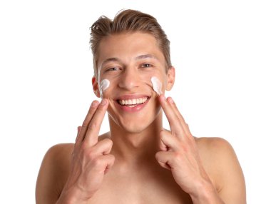 Beyaz arka planda yüzüne krem süren yakışıklı bir genç.