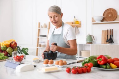 Üst düzey kadın mutfaktaki beyaz mermer masada yemek pişiriyor.