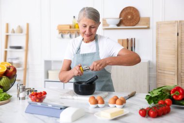 Üst düzey kadın mutfaktaki beyaz mermer masada yemek pişiriyor.
