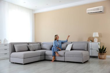 Evdeki koltukta uzaktan kumandayla klima kullanan bir kadın.