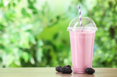 Plastik bardaktaki lezzetli milkshake ve dışarıdaki ahşap masadaki böğürtlenler.