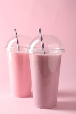 Pembe arka planda plastik bardaklarda lezzetli milkshake.