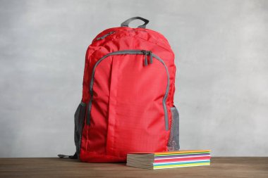 Kırmızı sırt çantası ve defterler gri arka planda tahta masanın üzerinde. Metin için boşluk