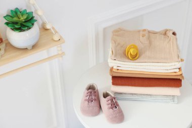 Beyaz masa içinde temiz bebek kıyafetleri ve aksesuarlar yığını. Mesaj için yer var.