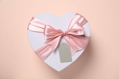 Soluk pembe arka planda boş etiketli kalp şeklinde bir hediye kutusu.