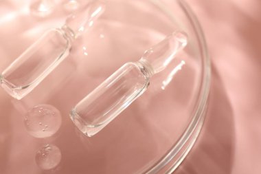 Kozmetik ürünlü cam ampuller ve pembe arka planda Petri kabı, yakın plan.