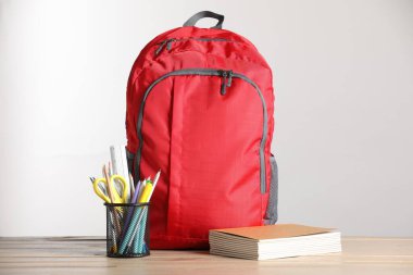 Kırmızı sırt çantası ve ahşap masa üzerindeki farklı kırtasiye malzemesi.
