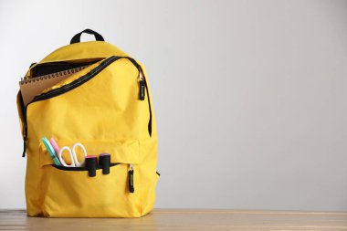 Açık gri arkaplan üzerinde kırtasiye malzemesi olan sarı sırt çantası, metin için boşluk