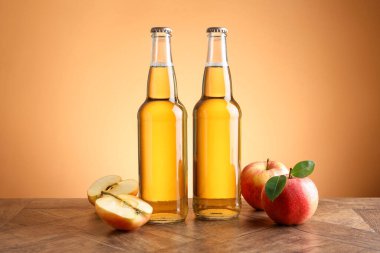 Cam şişelerde lezzetli elma şarabı ve ahşap masada portakal eğimli arka planda elmalar.