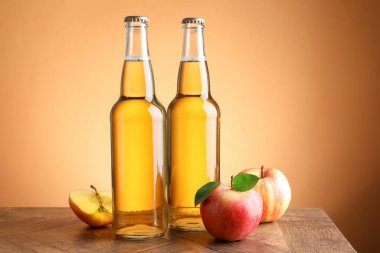 Cam şişelerde lezzetli elma şarabı ve ahşap masada portakal eğimli arka planda elmalar.