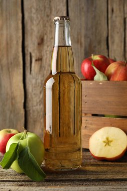 Cam şişede nefis elma şarabı ve ahşap masada elmalar, yakın plan.