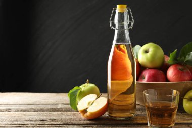 Şişede nefis elma şarabı, ahşap masada koyu gri arka planda cam ve elmalar. Metin için boşluk