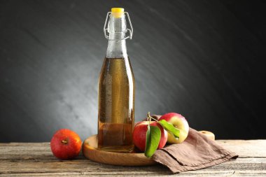 Cam şişede nefis elma şarabı ve ahşap masada koyu gri arka planda elmalar