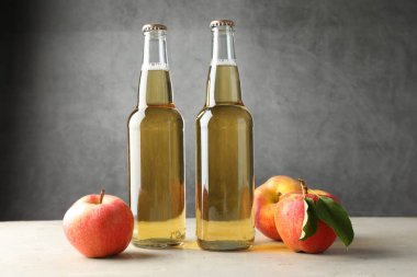 Cam şişelerde lezzetli elma şarabı ve gri arka planda elmalar.