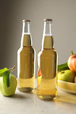 Cam şişelerde nefis elma şarabı ve gri masada hafif arka planda elmalar.