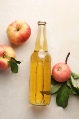 Cam şişede nefis elma şarabı ve bej masa üzerinde yeşil yapraklı elmalar, düz uzanmış.