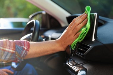 Salondaki yeşil mikrofiber bezle araba panelini silen adam, yakın plan.