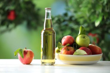 Cam şişede nefis elma şarabı ve açık havada beyaz ahşap masada elmalar.