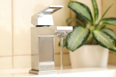 Su tasarrufu konsepti. Musluktan akan su akıntısı ve ev bitkisi kapalı, seçici odak