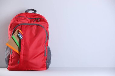 Işık duvarının yanındaki masada farklı kırtasiye malzemelerinin olduğu kırmızı sırt çantası. Metin için boşluk