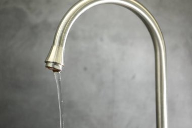 Su kavramını sakla. Gri arkaplandaki musluktan akan su akışı, yakın plan