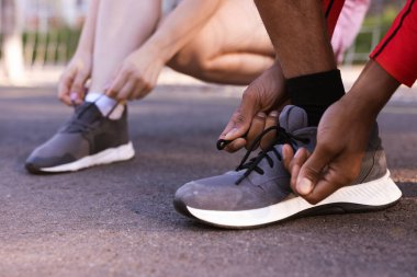 Stadyumda ayakkabı bağcıklarını bağlayan koşucular, yakın plan.