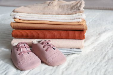 Yatakta temiz bebek kıyafetleri ve ayakkabılar yığını.