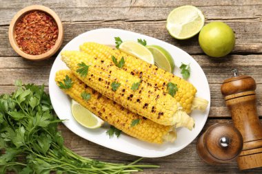 Lezzetli ızgara mısır koçanları maydanozlu ve ahşap masada limon dilimleri var.