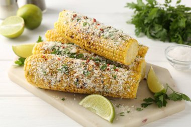 Lezzetli ızgara mısır koçanları maydanozlu, peynirli ve limon dilimli beyaz ahşap masa, yakın plan.