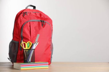 Kırmızı sırt çantası ve ahşap masanın üzerindeki farklı kırtasiye malzemesi. Metin için boşluk