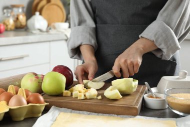 Elmalı turta yapıyorum. Mutfaktaki gri masada taze meyve kesen kadın, yakın plan.