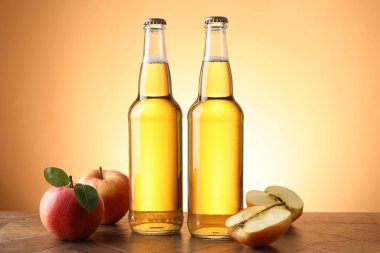 Cam şişelerde lezzetli elma şarabı ve ahşap masada portakal eğimli arka planda elmalar.